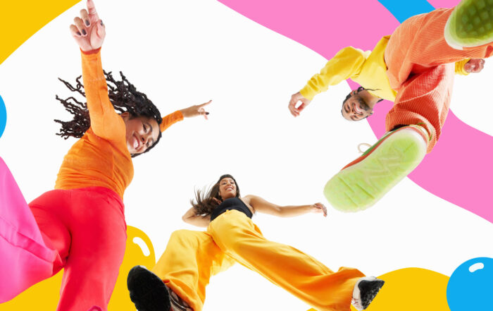 full length studio shot of three people looking down at camera smiling and dancing against colourful background