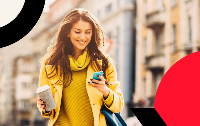 Person wearing yellow walking in the city while holding cellphone and coffee mug